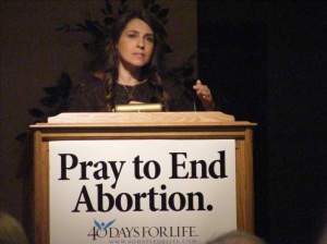 Woman at podium with sign saying Pray to End Abortion